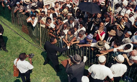 Picture taken from above of Martin Luther King Jr in a suit shaking hands with a crowd across a fence